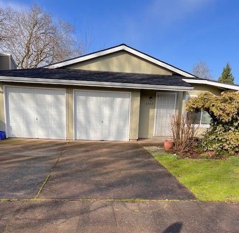 A single-story home with two garage doors and a small front yard on a sunny day.