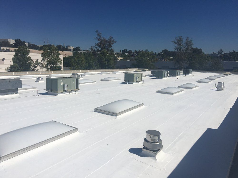 A bright white commercial rooftop under a clear blue sky, featuring several rectangular skylights and HVAC units.