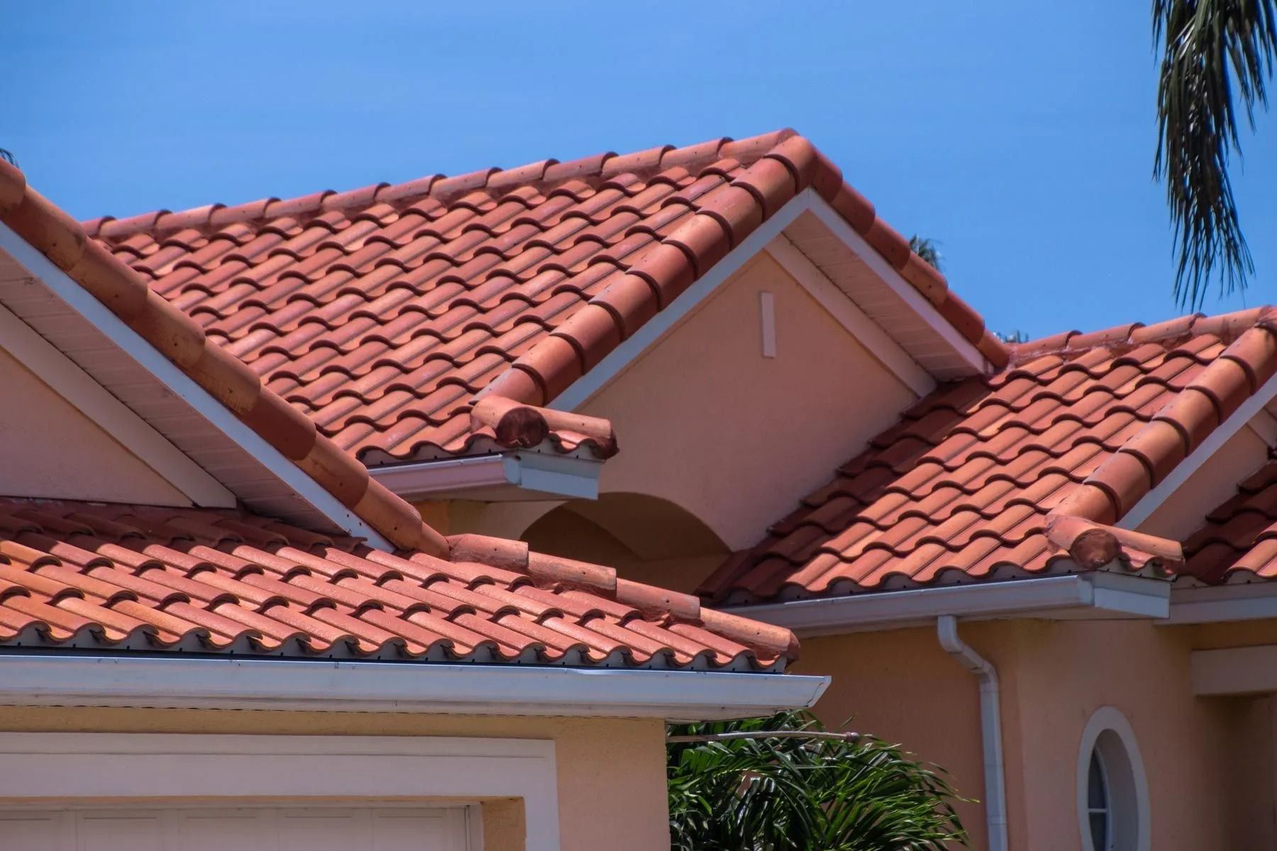 Close-up of a residential house roof with reddish-orange clay barrel tiles under a clear blue sky.