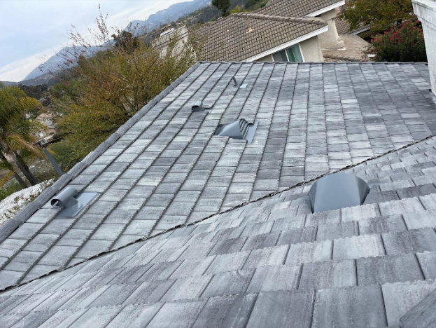 A high-angle view of a gray shingled roof with several roof vents and a distant view of hills and trees.