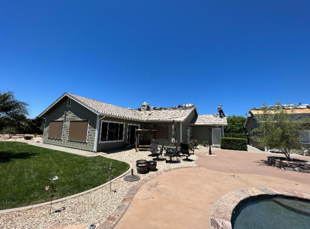 A green house with a roof under construction sits next to a pool area on a bright, sunny day.