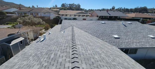 An elevated, straight-on view of gray asphalt shingle roofing on residential homes under a clear blue sky.