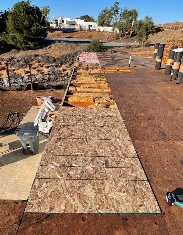Construction site showing partially installed OSB subflooring over exposed joists and insulation outdoors.