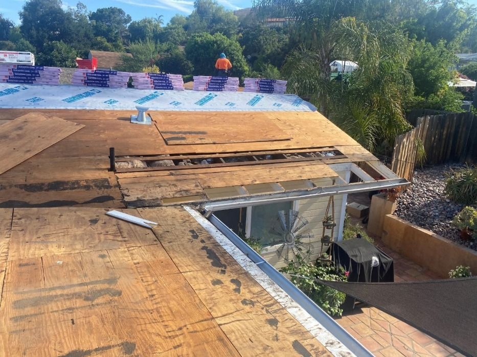 A partially reroofed home with exposed wooden decking, new underlayment, and a worker visible on the roof.