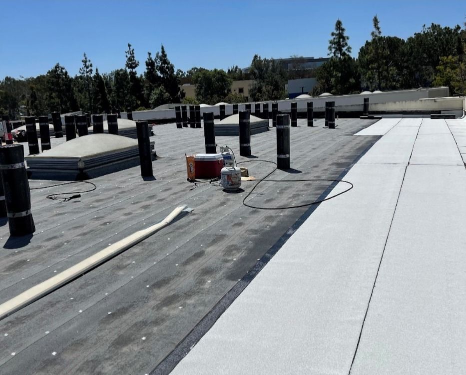 A commercial flat roof under construction, showing dark membrane sections and a freshly applied, light-colored surface.