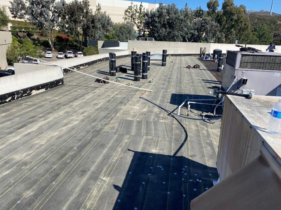 A view from a rooftop featuring a gray membrane surface, several dark ventilation pipes, and a large HVAC unit.