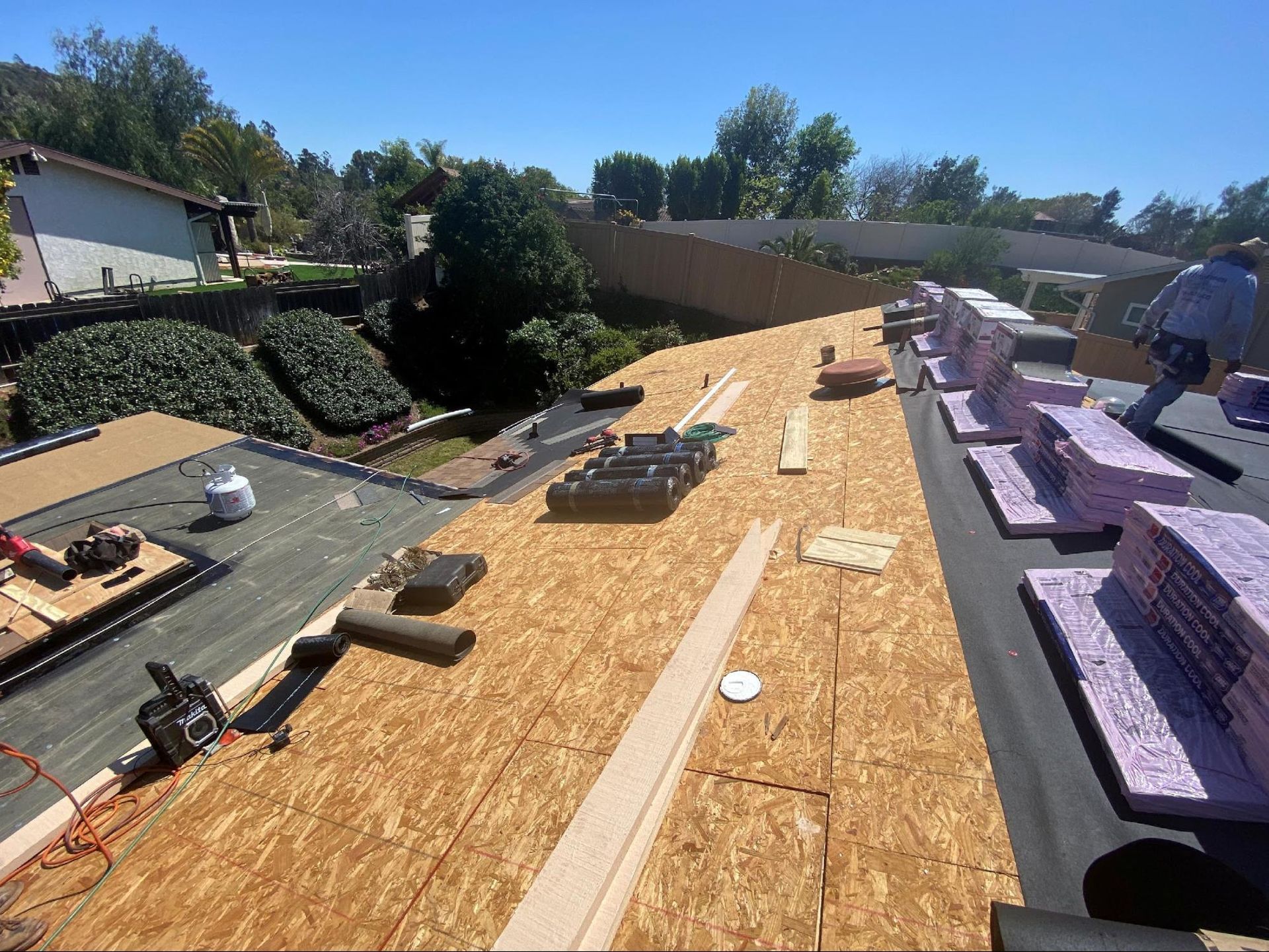 A construction worker on a residential roof installing plywood sheathing and rigid foam insulation boards.