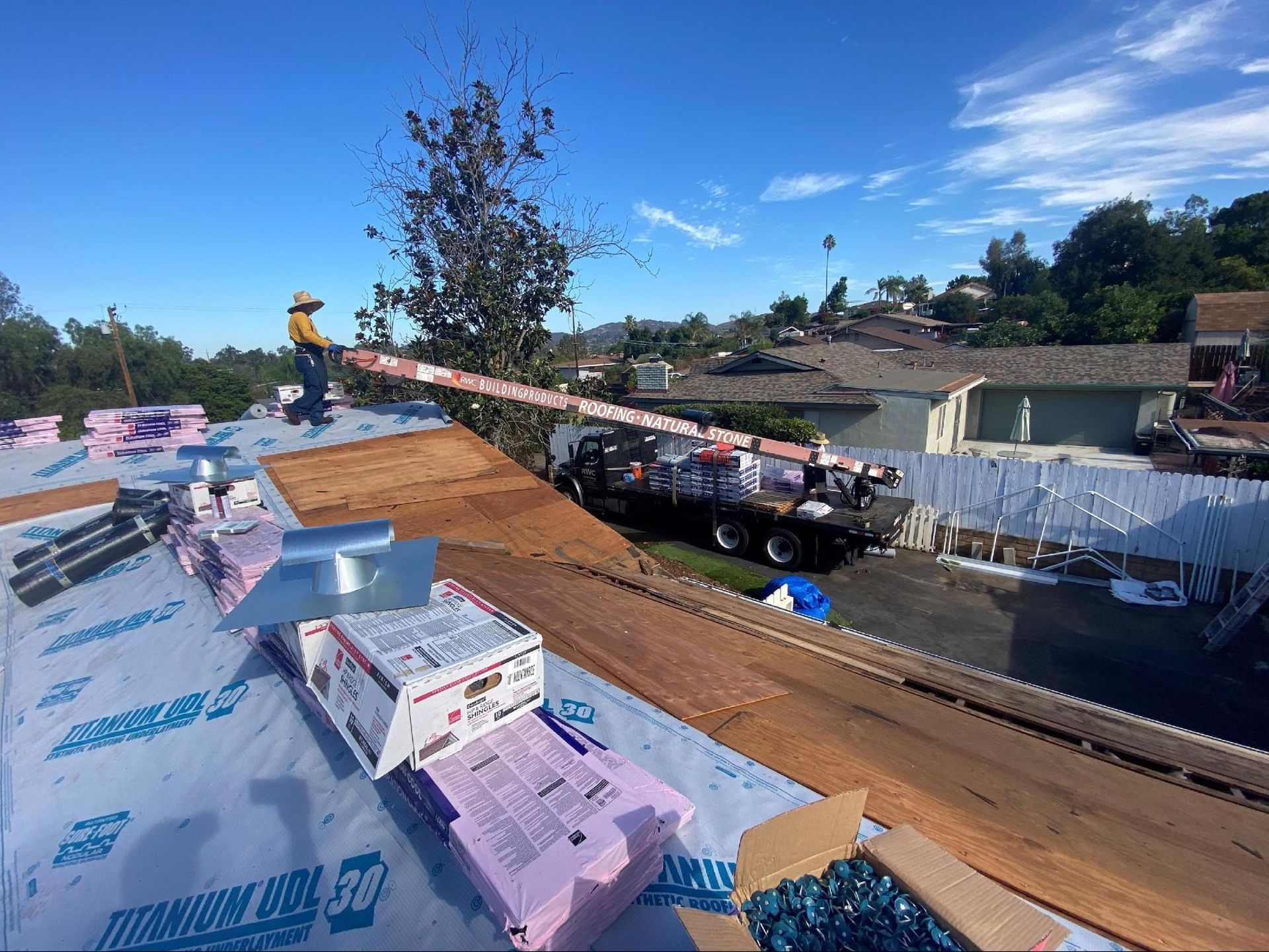 A person stands on a residential roof during a renovation, with construction materials visible nearby.
