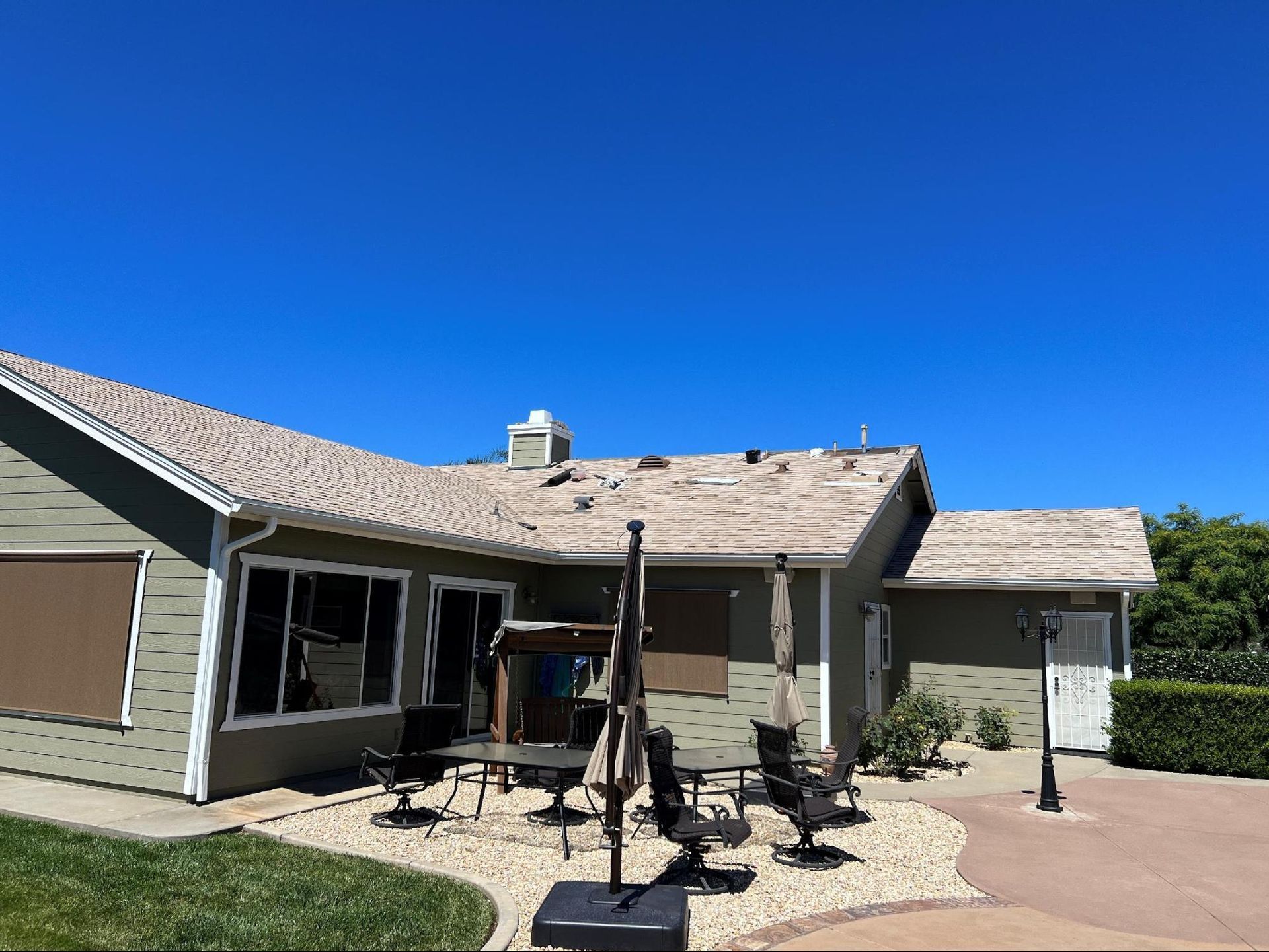 Patio with outdoor furniture next to a single-story house under a clear blue sky.