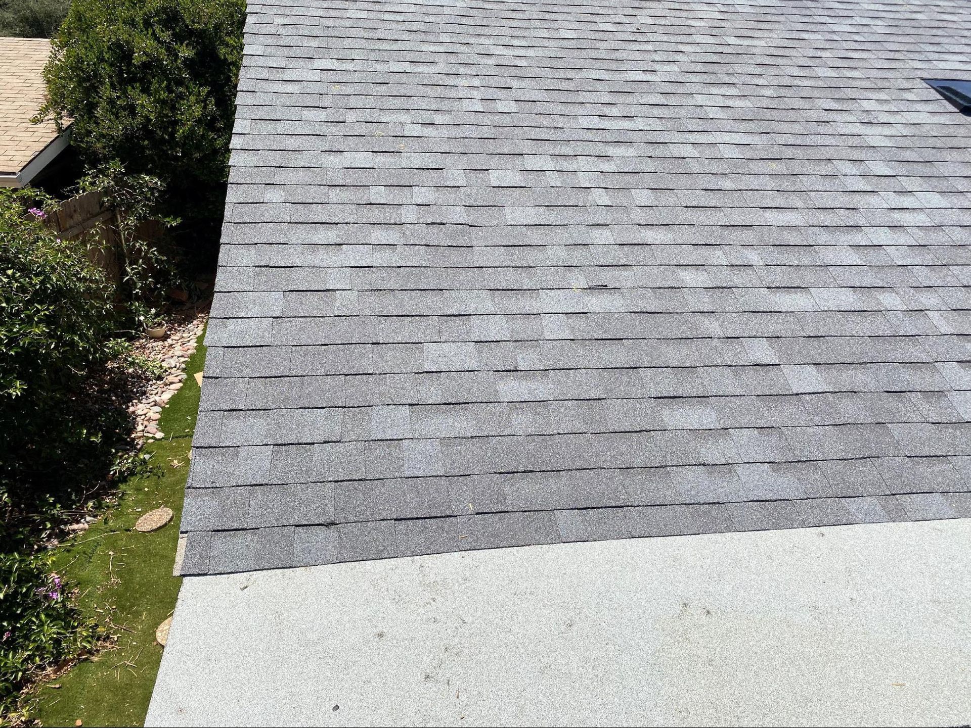 A high-angle view of a gray asphalt shingle roof transitioning to a flat, light-colored gravel surface.
