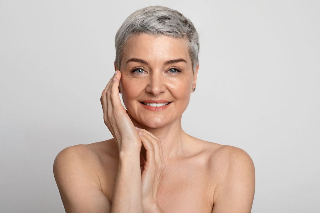 A woman with short hair is smiling and touching her face.