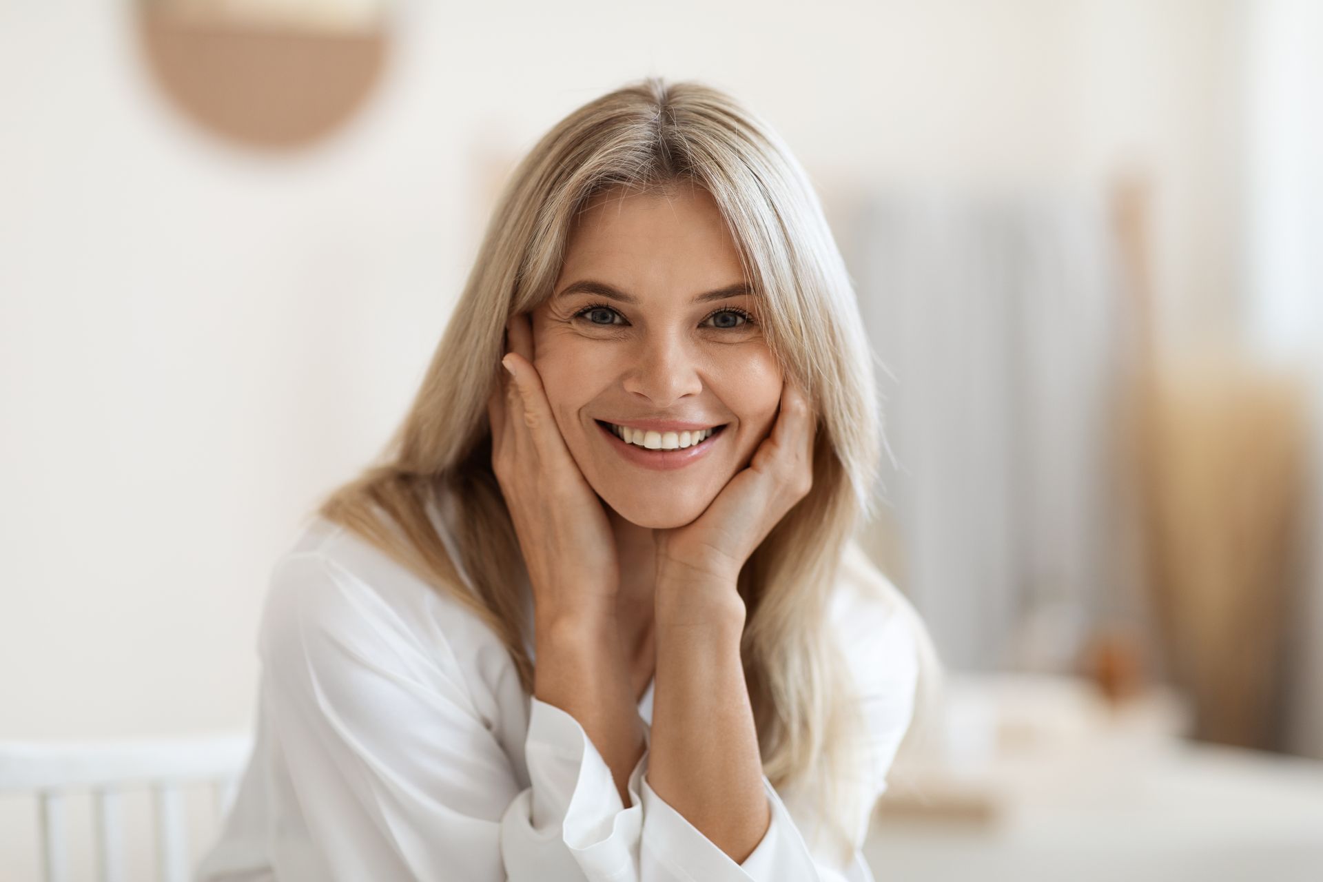 A woman is smiling with her hands on her face.