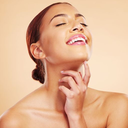 A woman is smiling and touching her neck with her hands.