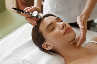 A woman is getting an airbrush treatment on her face.