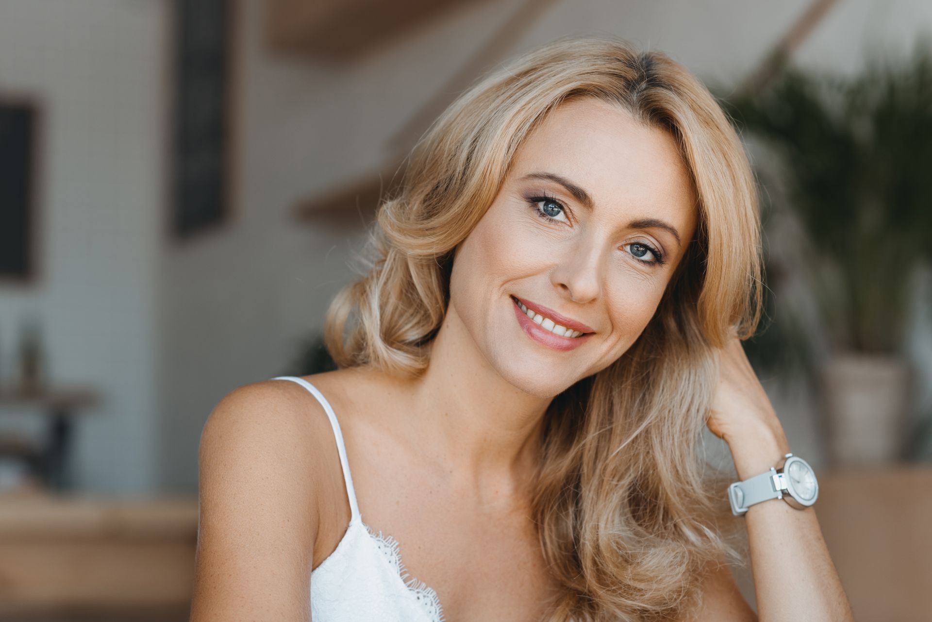 A woman in a white tank top is smiling and wearing a watch.