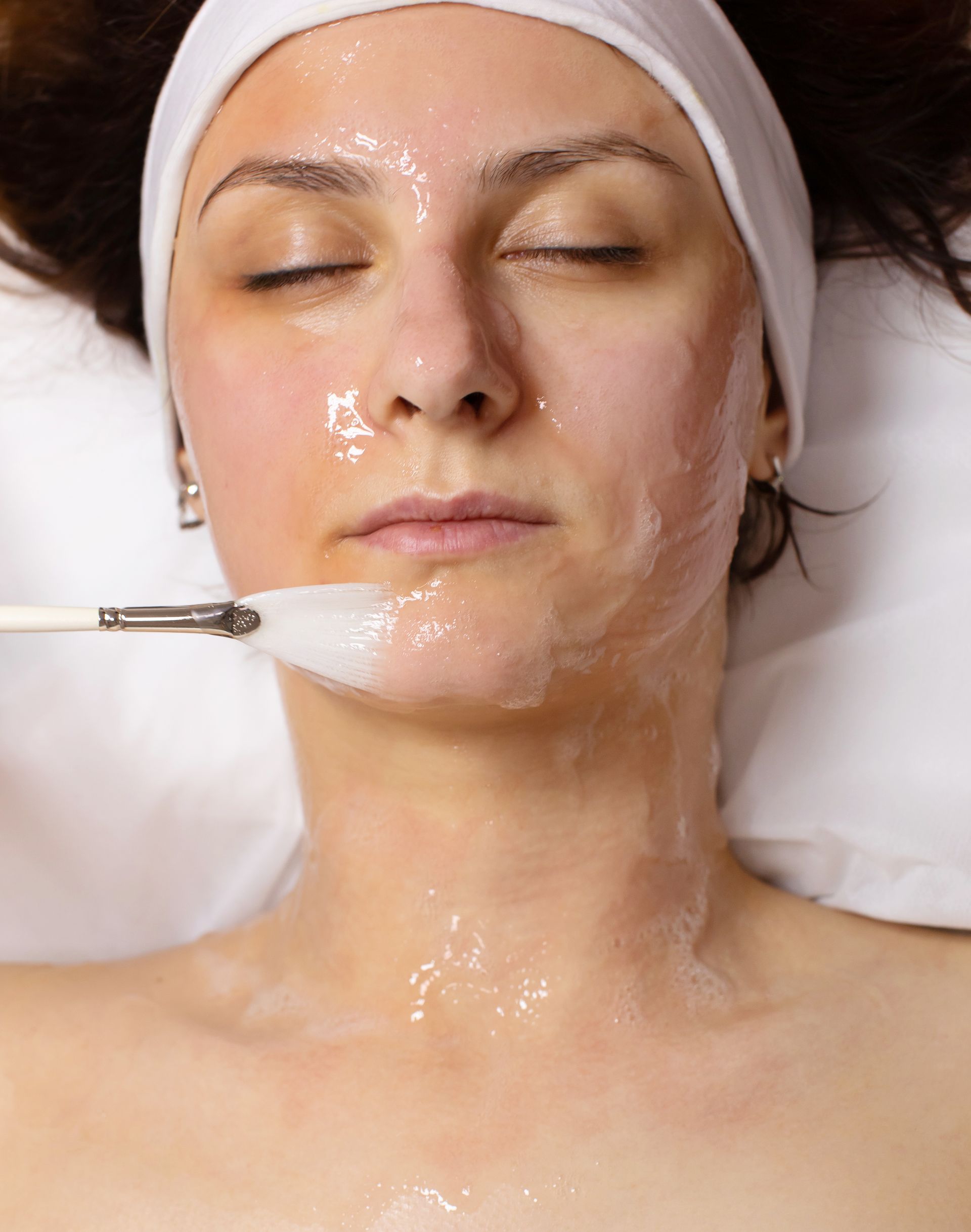 A woman is getting a facial treatment with a brush on her face.