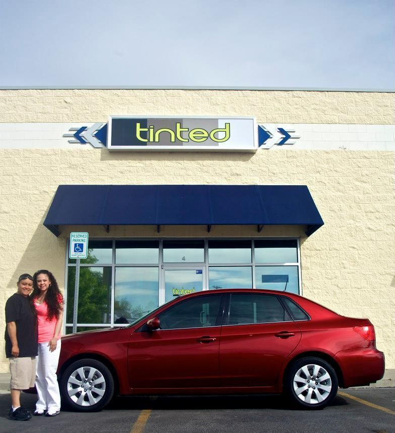 A red car is parked in front of a tinted store