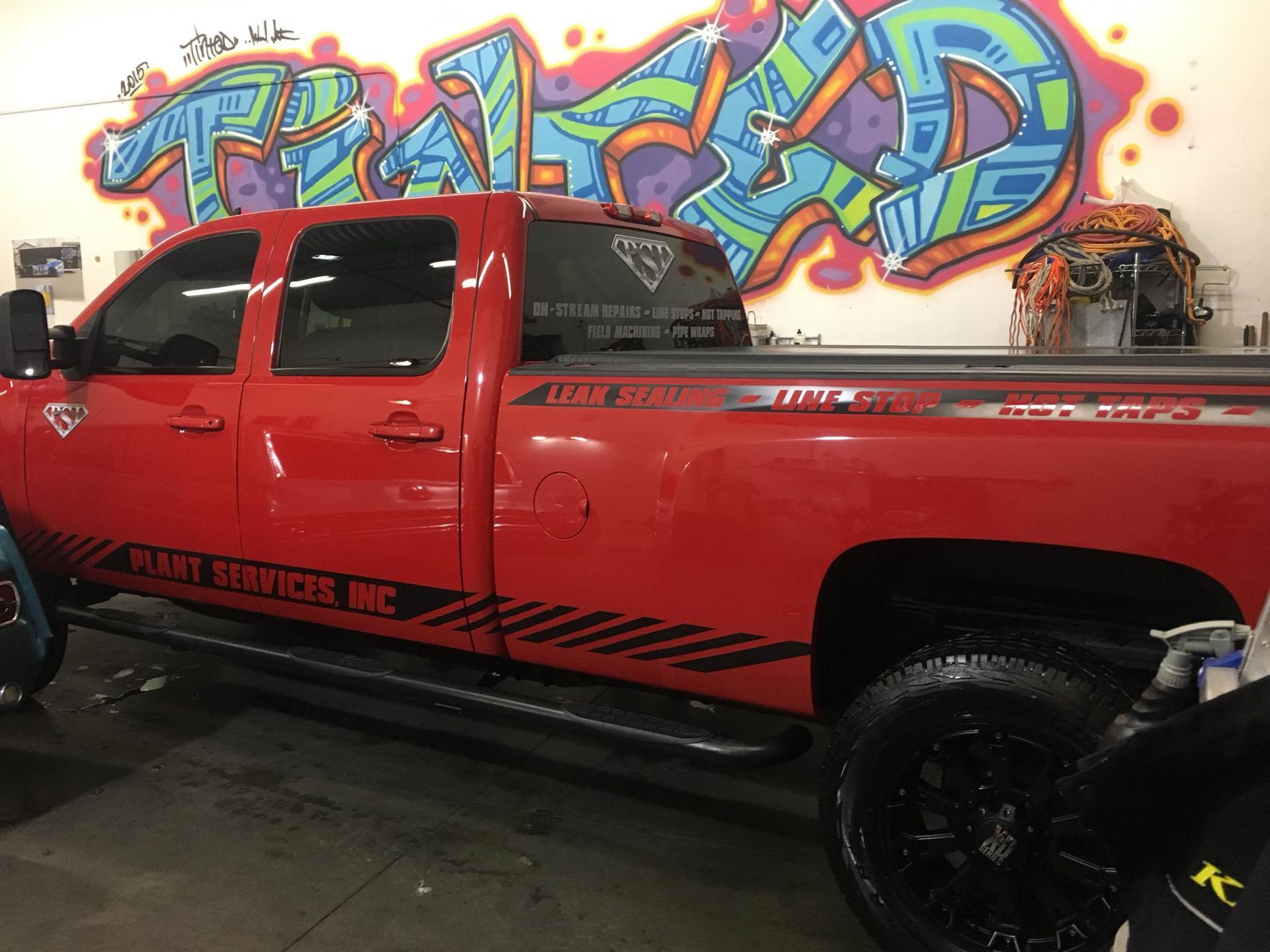 A red truck is parked in front of a wall with graffiti on it.