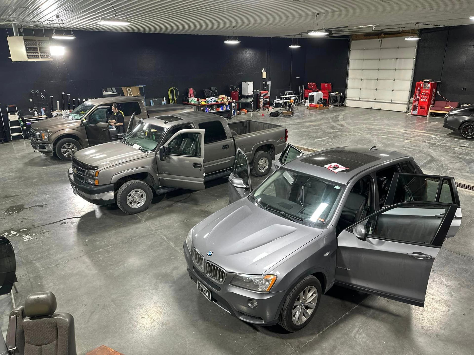 A row of cars are parked in a garage with their doors open.