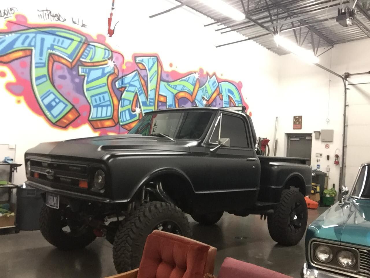 A truck is parked in a garage with graffiti on the wall behind it.