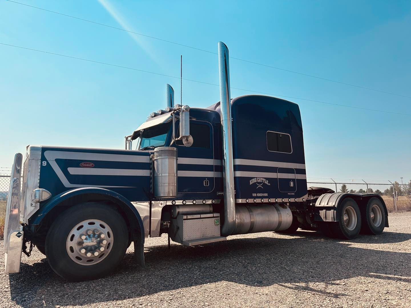 A blue semi truck is parked in a gravel lot.