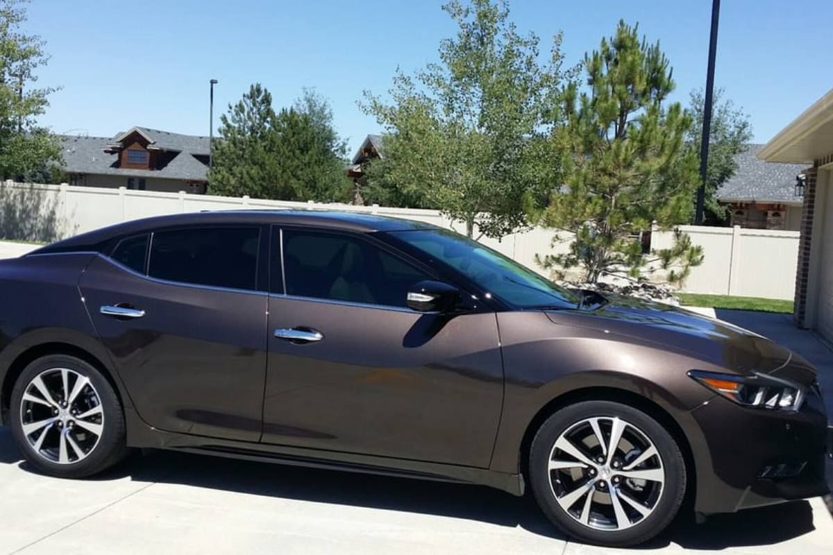 A brown car is parked in a driveway in front of a house.