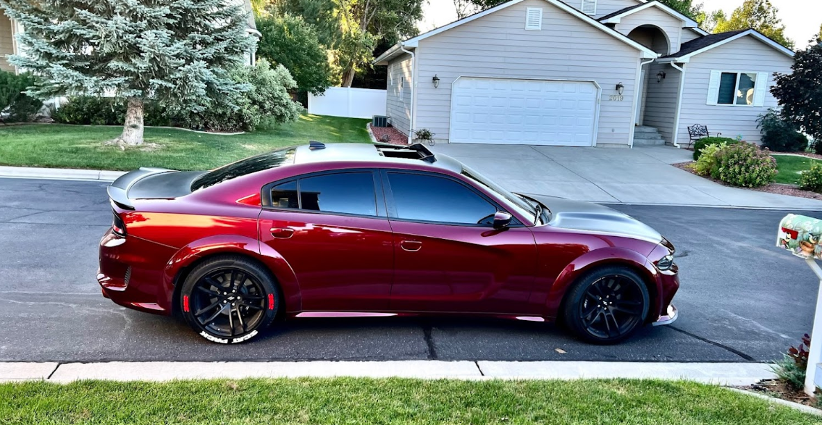 A red dodge charger is parked in front of a house.