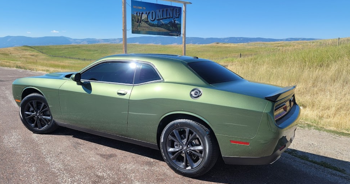 A green dodge challenger is parked on the side of the road.