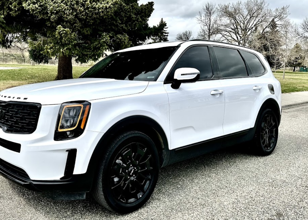 A white suv is parked on the side of the road next to a tree.
