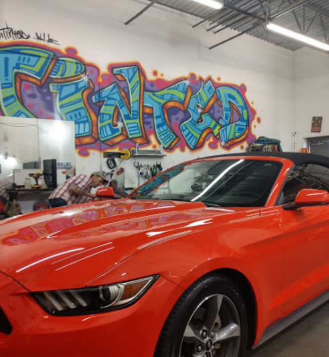 A red mustang is parked in a garage with graffiti on the wall behind it