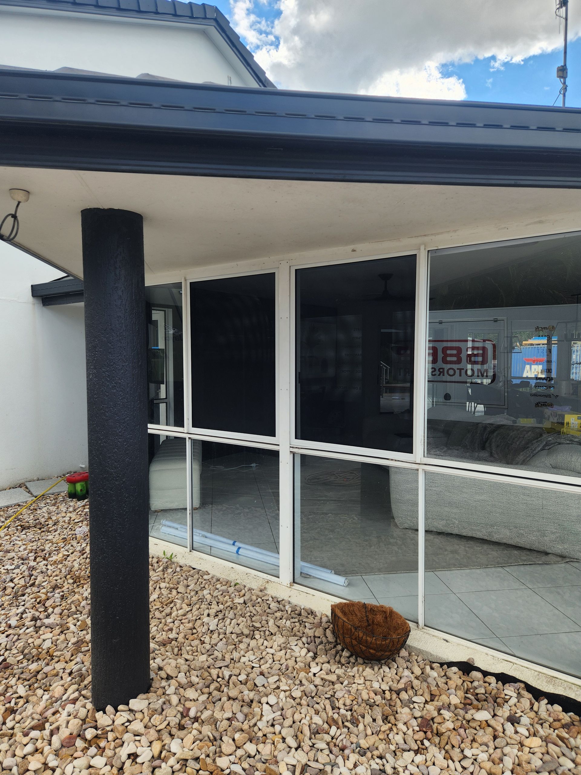 Glass-walled building exterior with black trim, a black pillar, and a gravel bed — Smart Screens Qld in Ormeau, QLD