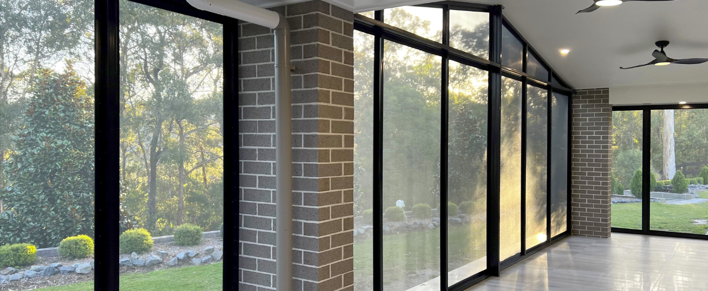 Interior with floor-to-ceiling windows and brick columns, overlooking a green yard and trees — Smart Screens Qld in Ormeau, QLD