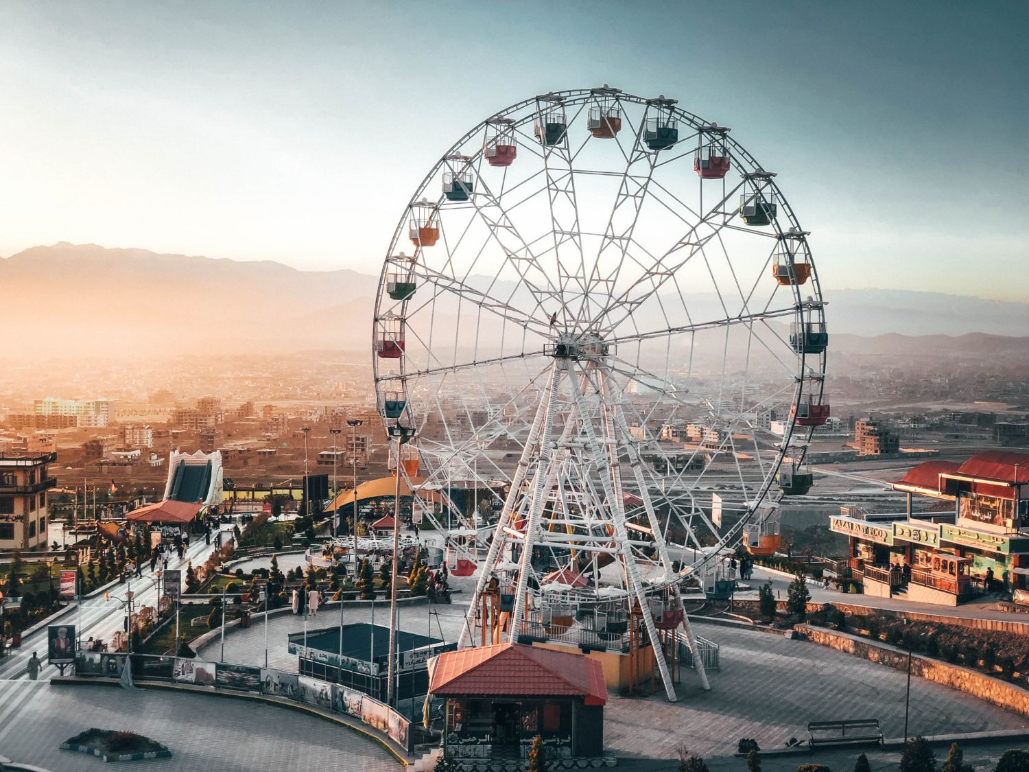 Ferris wheel at amusement park at sunset, overlooking a city.
