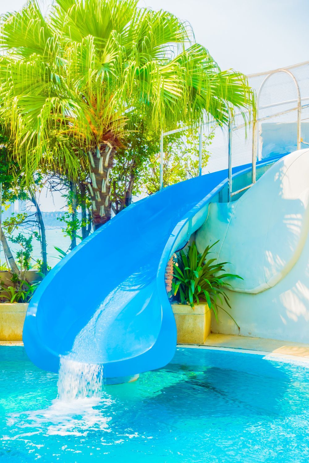 Blue water slide emptying into a pool, with palm trees in the background.