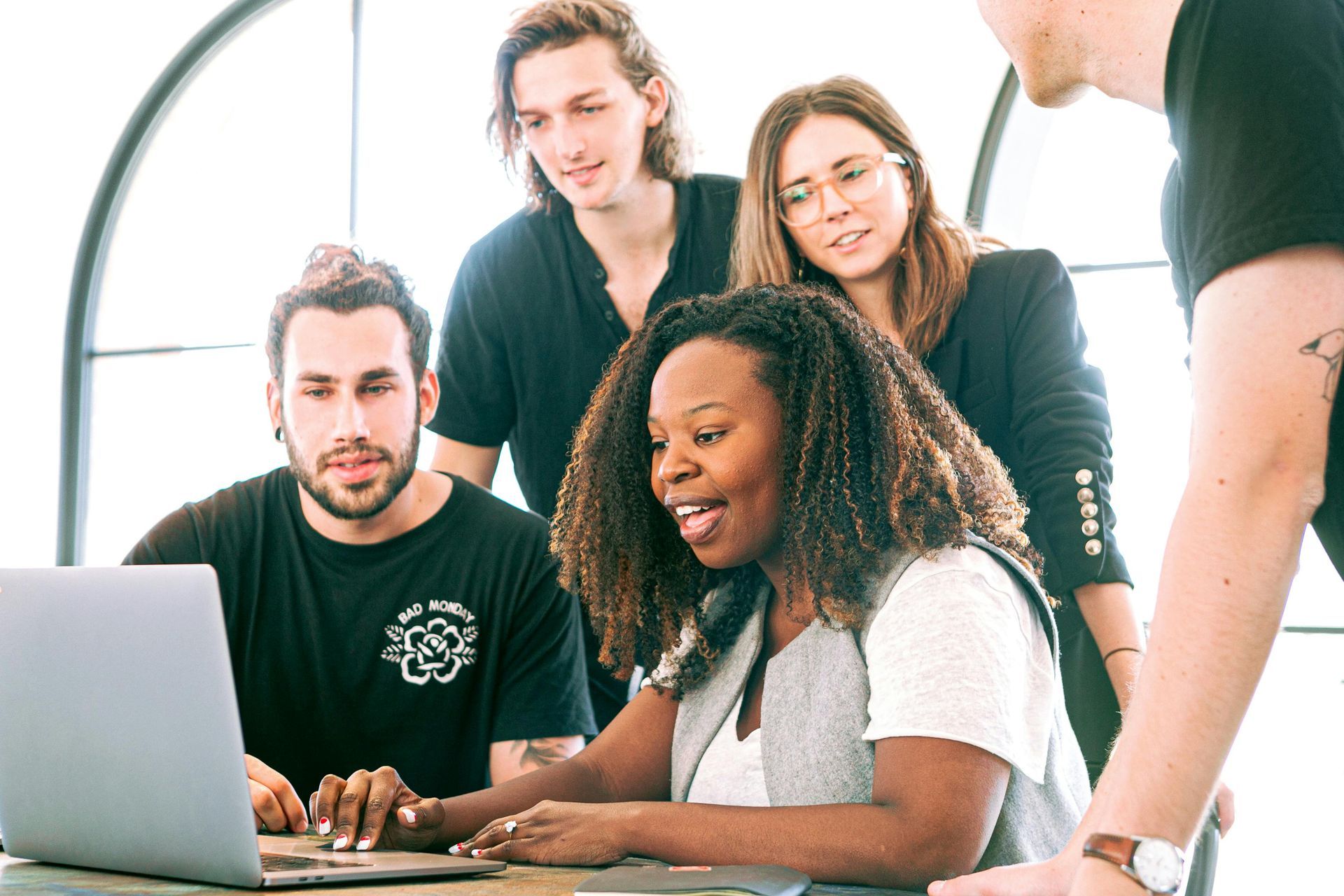 A group of four professionals collaborates around a laptop in a bright office space.