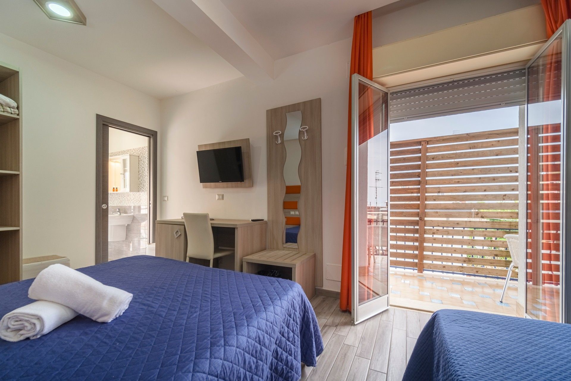 A hotel room with two beds, a desk, a television and a balcony.