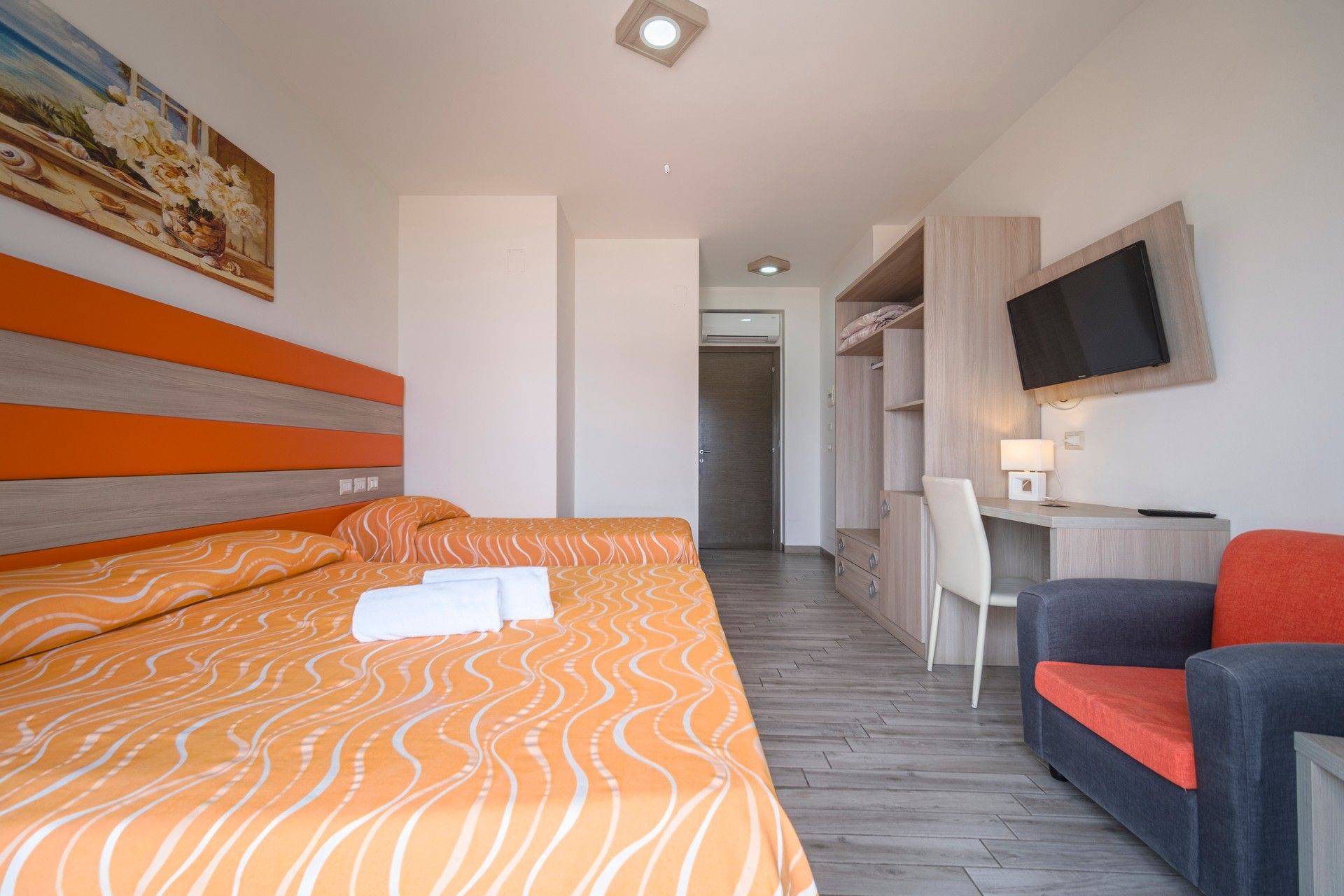 A hotel room with a bed, chair, desk and television.