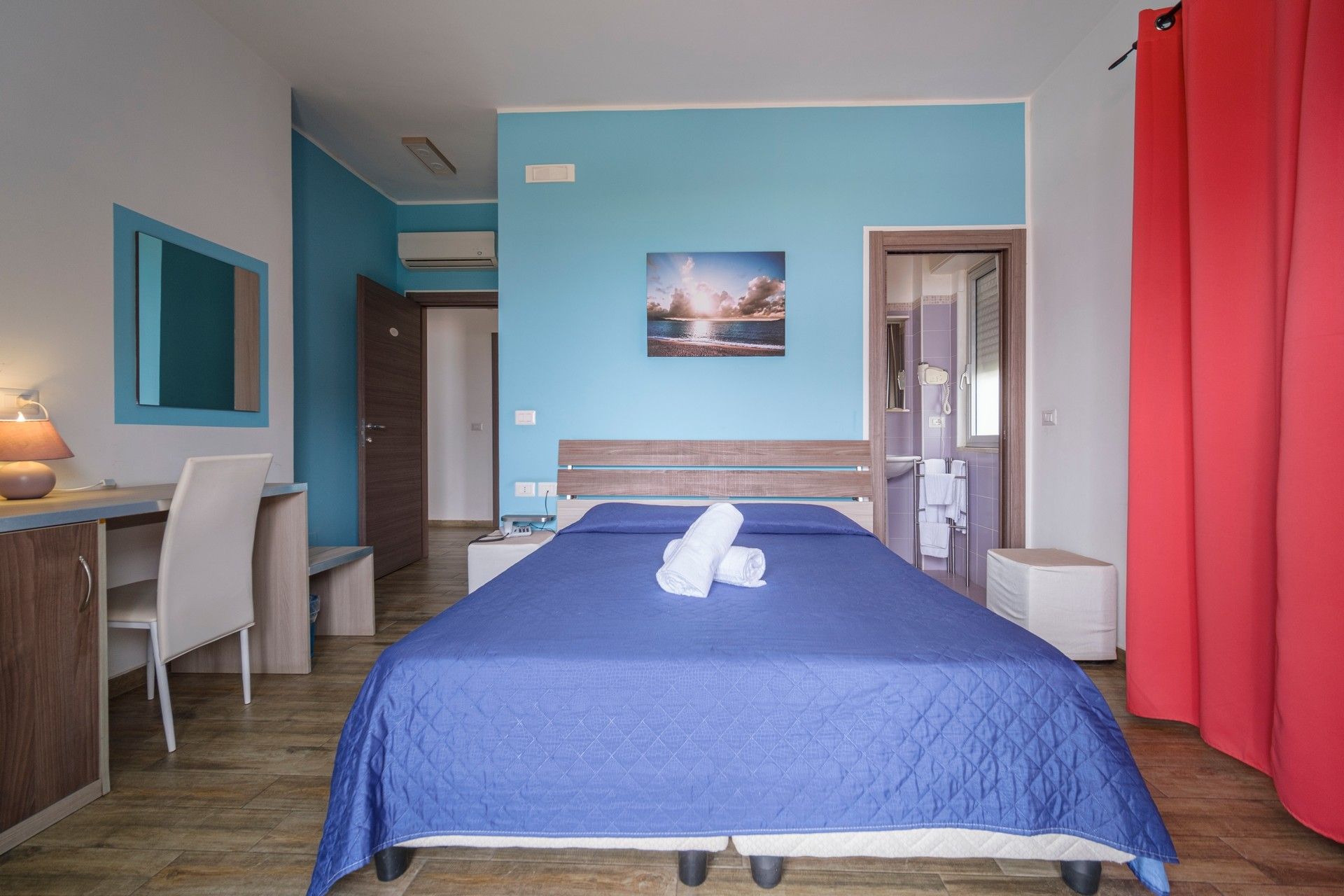 A hotel room with bed, desk, chairs and television.