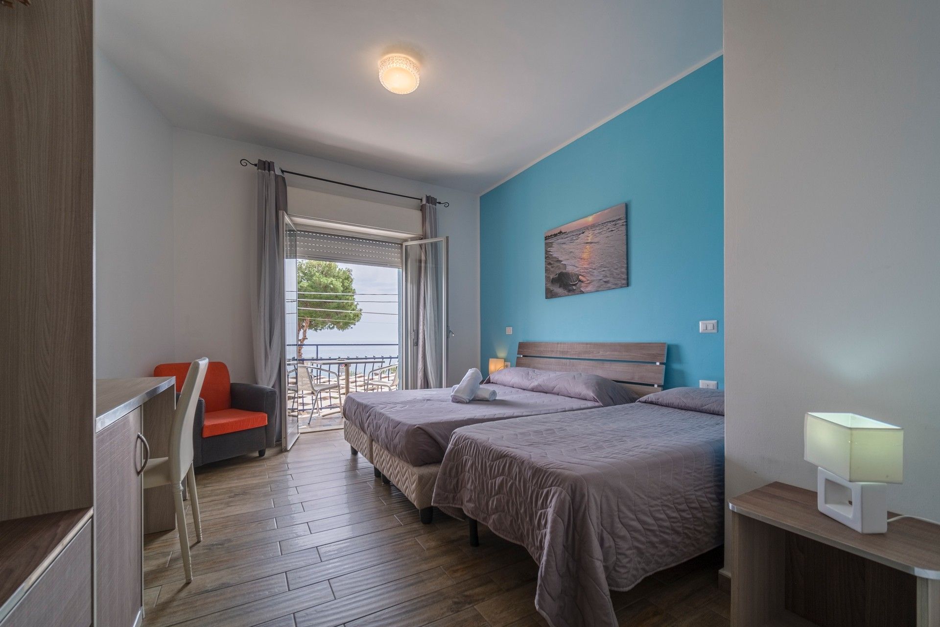 A hotel room with two beds, a chair, a desk and a balcony.