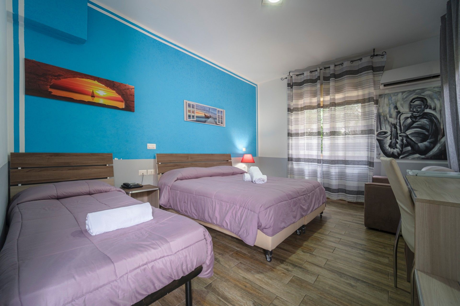 A hotel room with two beds and a blue wall.