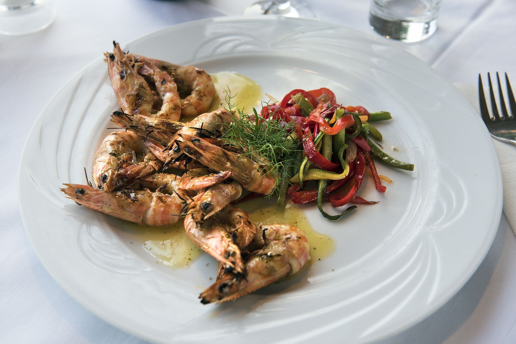 A white dish topped with shrimps and vegetables on a table.