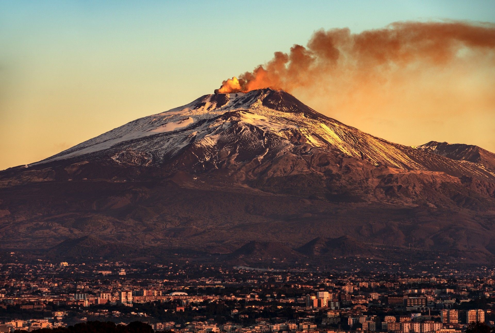 A volcano billowing smoke and a city in the foreground