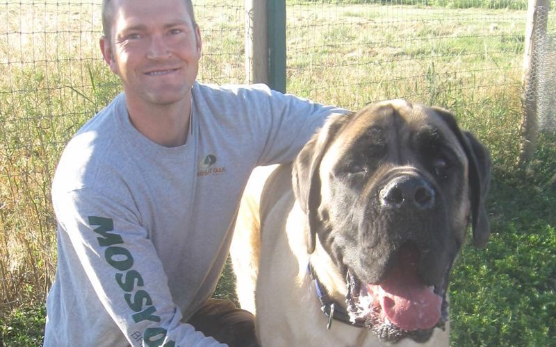 A man standing next to a large dog with mossy on his sleeves