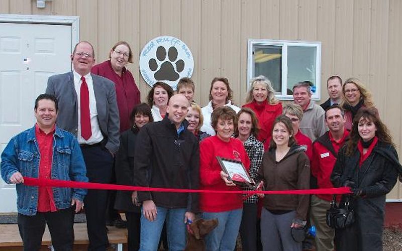 A group of people standing in front of a building holding a red ribbon