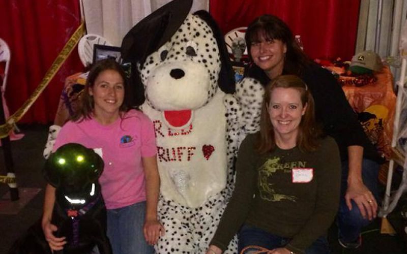 Three women are posing for a picture with a dalmatian mascot named ruff
