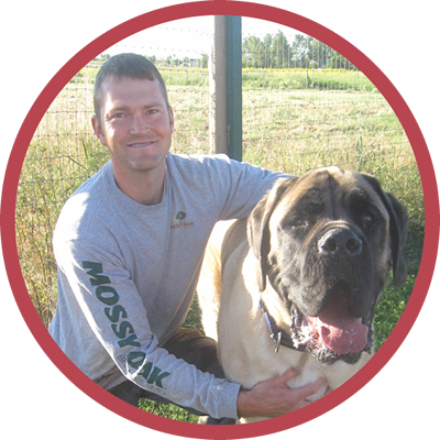 A man in a mossyoak shirt holds a large dog