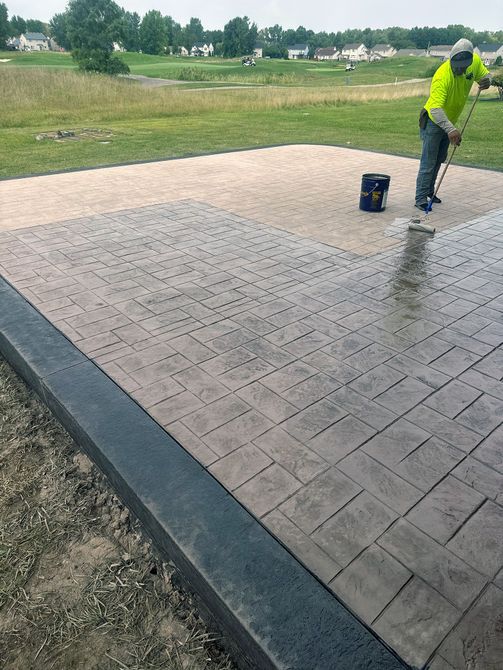 A man is painting a concrete patio with a broom.