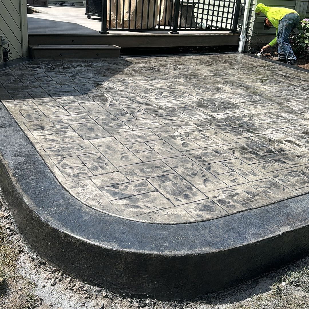 A man is working on a concrete patio next to a deck.