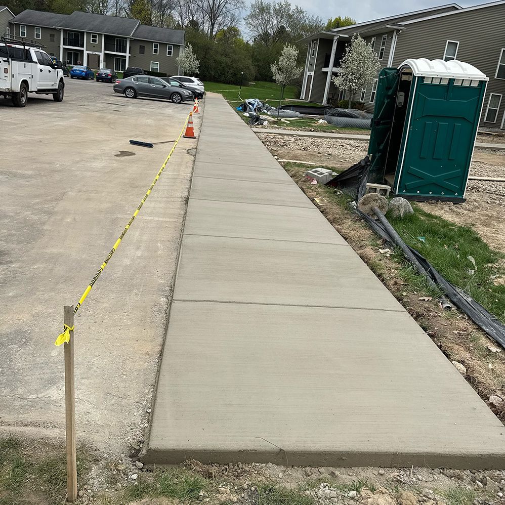 A concrete walkway is being built next to a green portable toilet