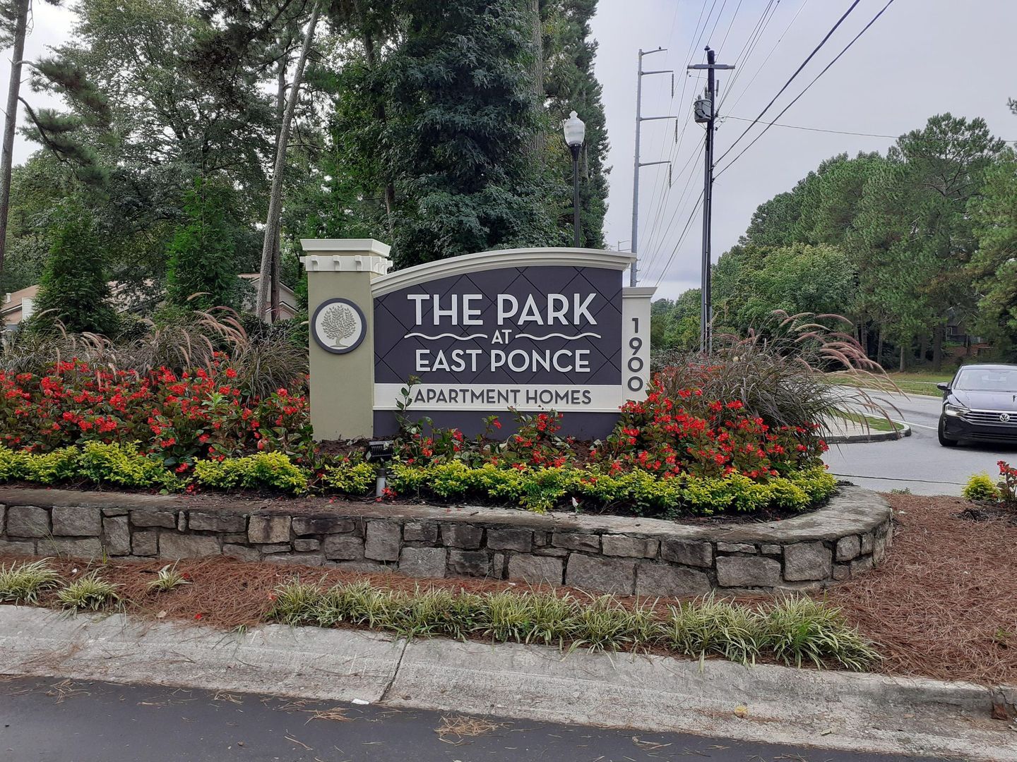 Sign for The Park at East Ponce Apartment Homes, with flowers and a car on a cloudy day.